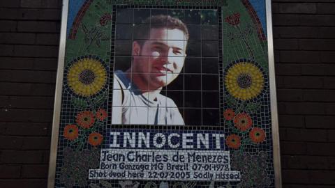 Memorial mosaic of Jean Charles de Menezes, featuring his portrait framed by colorful flowers and the word "INNOCENT" in bold letters beneath. The text below includes his birth details and states he was "sadly missed".