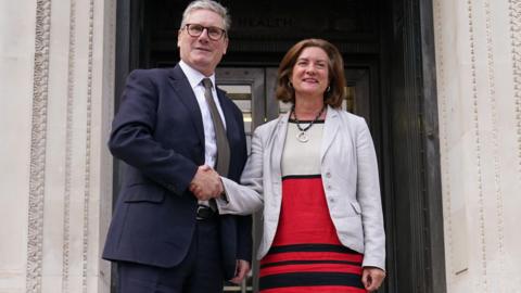 A smiling Sir Keir Starmer and Eluned Morgan shake hands on the steps of the Welsh government building in Cathays Park, Cardiff