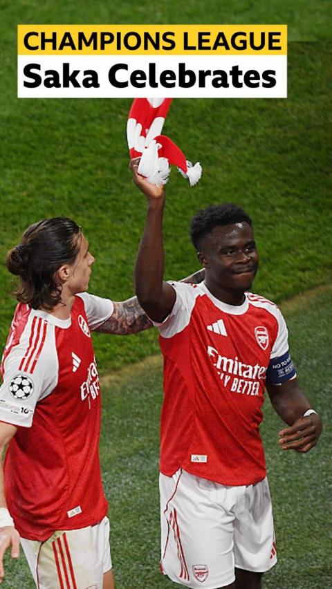 Bukayo Saka holds up an Arsenal scarf with Calafiori standing next to him