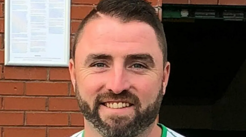 A man with brown hair and a beard smiling at the camera.