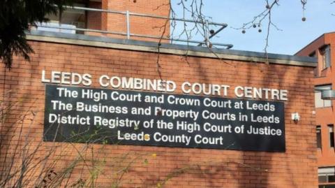 The outside of Leeds Crown Court. A red-brick building bearing the words: "Leeds Combined Court Centre; The High Court and Crown Court at Leeds; The Business and Property Courts in Leeds; District Registry of the High Court of Justice; Leeds County Court