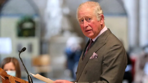 A side view of King Charles III standing at a lectern, with him looking to his left