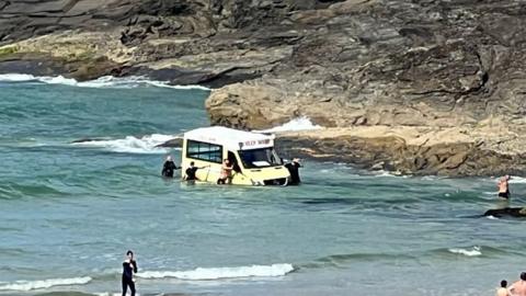 Ice cream van with water above its wheels as people try to stop it going further out to sea