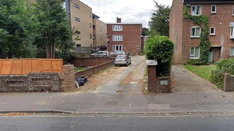 Drive with path and hedging with flats at the end. Also a brown fence and multiple cars outside