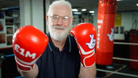 Peter Rogers, a bearded man, holding up his boxing gloves, smiling in the ring and celebrating his £1m lottery win