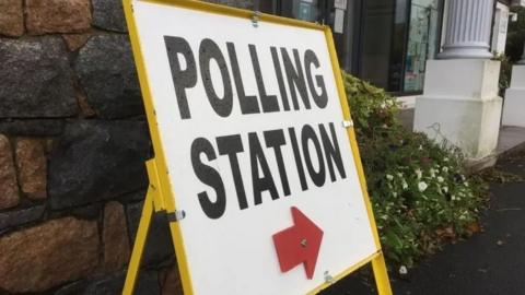A polling station sign with a red arrow and framed in yellow.