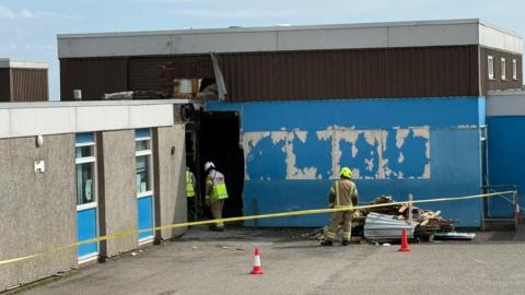 Firefighters behind a yellow cordon investigate the damage to Dales Park primary school