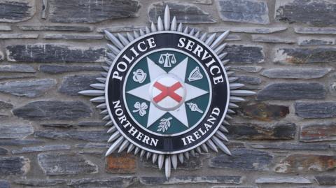 PSNI crest that says Police Service of Northern Ireland - on a stone wall. 