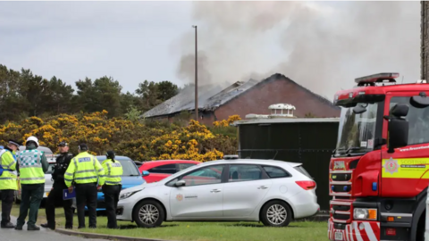 Na poilis aig làrach teine taobh a-muigh Gearastan Dheòrsa 