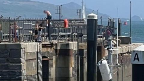 Several young people climb over the railings of a granite pier.