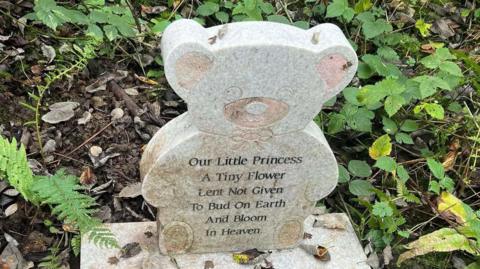 A grave found in a nature reserve, made from carved granite and in the shape of a teddy bear. 