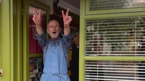 Joe Public gives the peace sign outside his shop