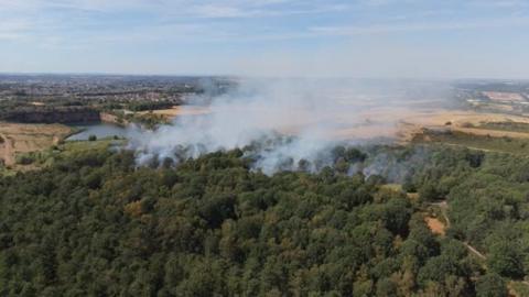 A photo from above of a large area woodland with smoke rising above it.