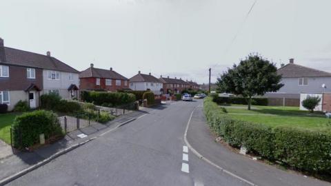 A number of houses are pictured on the left hand side of the road in this generic photo. The street goes from the bottom of the image up to around the centre of the photo.