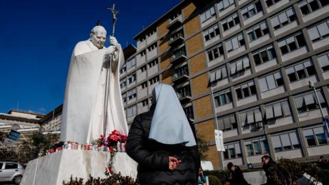 A nun looks up at a statue of late Pope Jon Paul II outside Gemelli Hospital in Rome