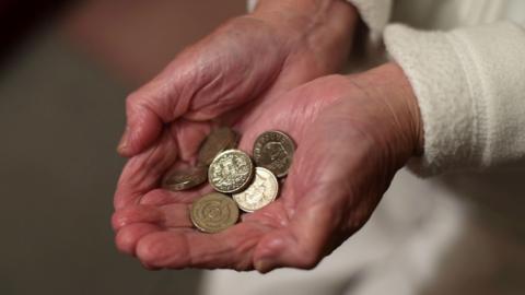 An old person holding some pound coins.