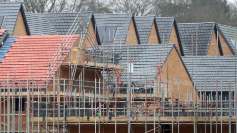 Generic shot of a building site where houses are being constructed. Tiled roofs can be seen as well as lots of scaffolding