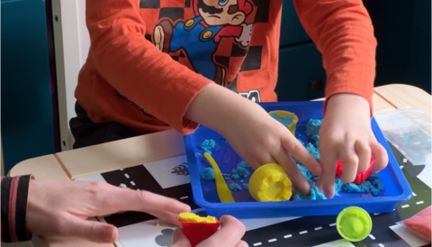 A boy in an orange Mario top plays with blue magic sand