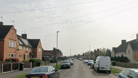 A Google streetview image of a long residential road with houses on both sides of the road. Cars and a van can also be seen parked on both sides.