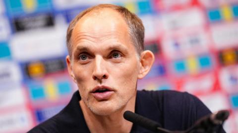 Tuchel speaking at conference, wearing black polo.