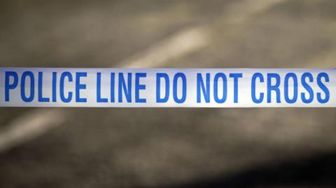 A police tape is stretched across a road with the words police line do not cross