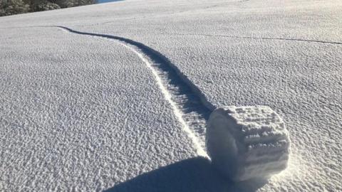 a snow roller on a snowy hill side with a track behind it.