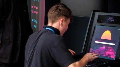 A teenage boy wearing a black polo top plays on an electronic gambling machine with his back to the camera.