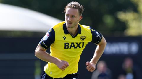 ben davies runs with his arms swinging by his sides. he looks to his right and wears a yellow shirt with navy sleeves and a navy collar.