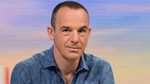 Martin Lewis wearing a blue shirt in front of a blue and orange background