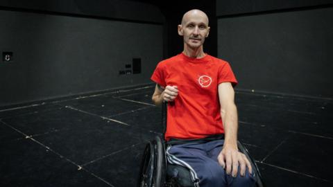 Marc Brew in a red T-shirt, smiling at the camera