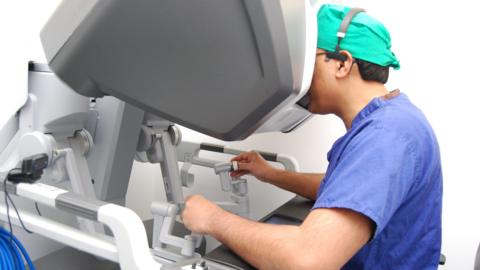 A surgeon in blue scrubs operates a surgical robot.