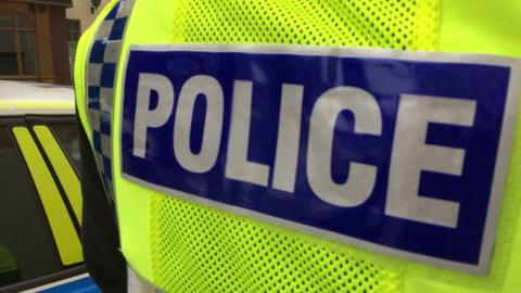 Back of luminous yellow hi-vis police jacket with the word police in white capital letters on a blue rectangular background.