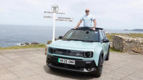 A man stands in a car with a retractable roof by a sign for Land's End