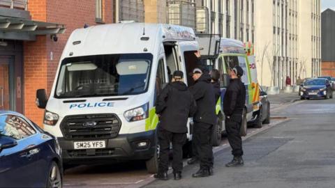 Four police officers standing in front of two police vans on a residential street