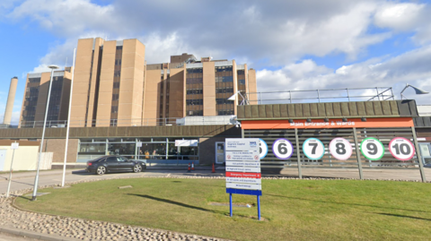 The front entrance to Raigmore Hospital with signs showing numbers and colours of different zones inside the large building.