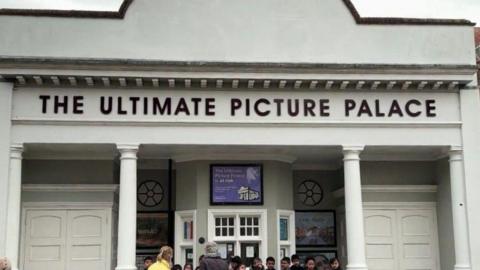 People gathering in front of the Ultimate Picture Palace on an overcast day.