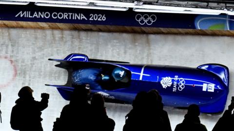A blue bobsleigh with the Team GB logo on it sliding down a track.