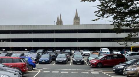 The multi-storey car park, with cars parked on the ground floor and outside and the top of Truro Cathedral visible behind