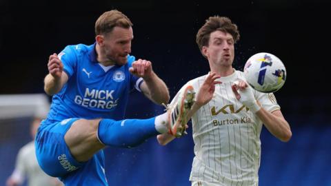 Peterborough defender Tom Lees clears a ball in front of Burton's Jake Beesley