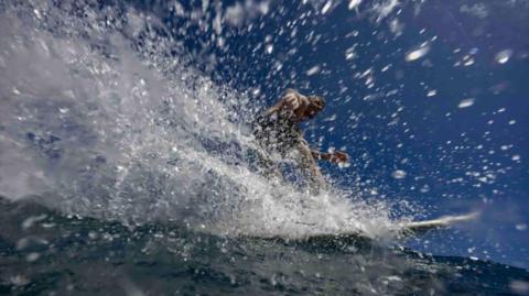 A surfer performs a cutback on a critical section of a wave creating a spray of water as they head back to the pit with a look of satisfaction and joy on their face.