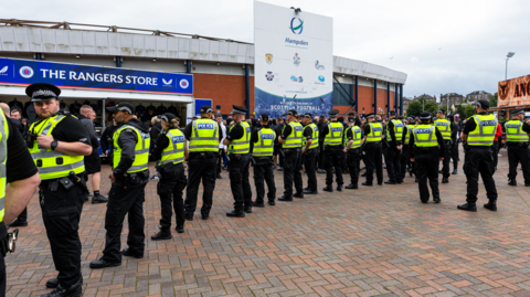 A line of police officers form a human barrier in front of Rangers supporters standing outside Hampden stadium