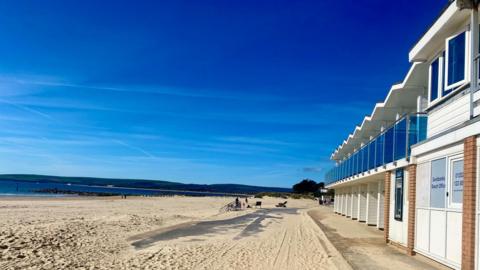 Blue sky over a beach lined with newly built beach huts. 