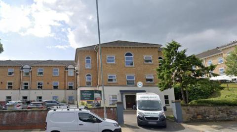 External view of Park House Care Home in Birkenhead showing an ambulance and driving out of the car park and a white transit van park in the street outside the entrance