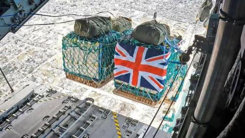 Humanitarian aid including water, rice, cooking oil, flour, tinned goods and baby formula wrapped in a Union Flag is airdropped over Gaza from a RAF A400M aircraft.