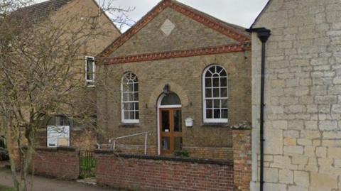 Exterior image of the Church building - with a triangle roof  and white oval glass windows with white frames.