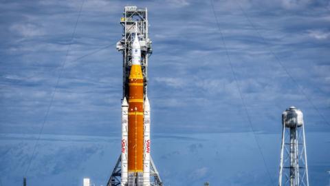 The Artemis II spacecraft, with a giant orange rocket, docked at a launch pad