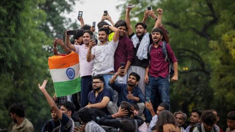 About a dozen people stand on an elevated platform celebrating, one holding an Indian flag