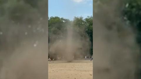 irking cloud of dust in a dry field with trees in the background.
