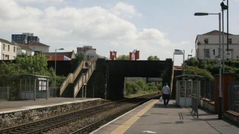 The photo shows both platforms at Lawrence Hill Station, taken from platform one looking across the tracks towards platform two. In the distance can be seen the steps to platform two, currently the only means of accessing it. A man holding a plastic bag can be seen walking away from the camera on platform one.