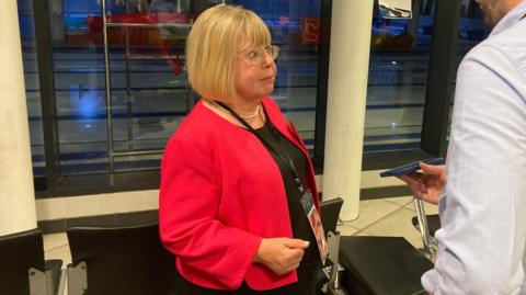 Blaydon and Consett MP Liz Twist. She is being interviewed by a reporter who is holding a phone. Twist is wearing a glasses and a red top. She has blonde hair and is wearing a lanyard.